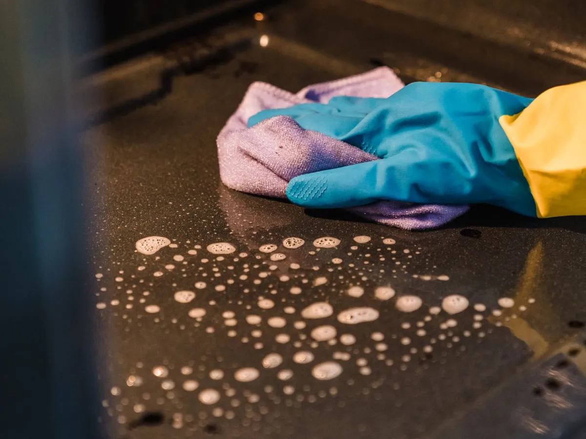 Gloved hand scrubbing the inside of an oven with a soapy cloth