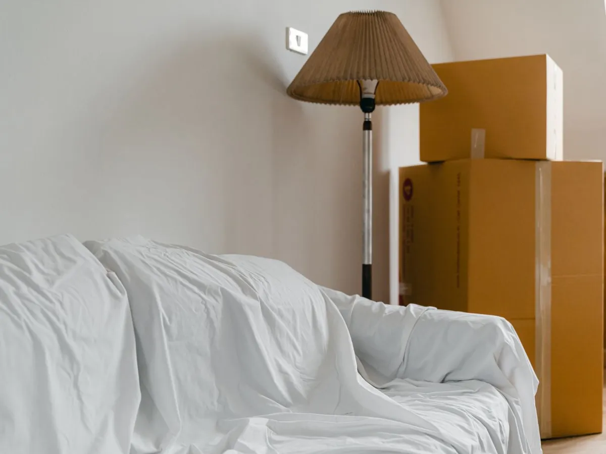 Sheet-covered sofa and packed moving boxes in a room being emptied