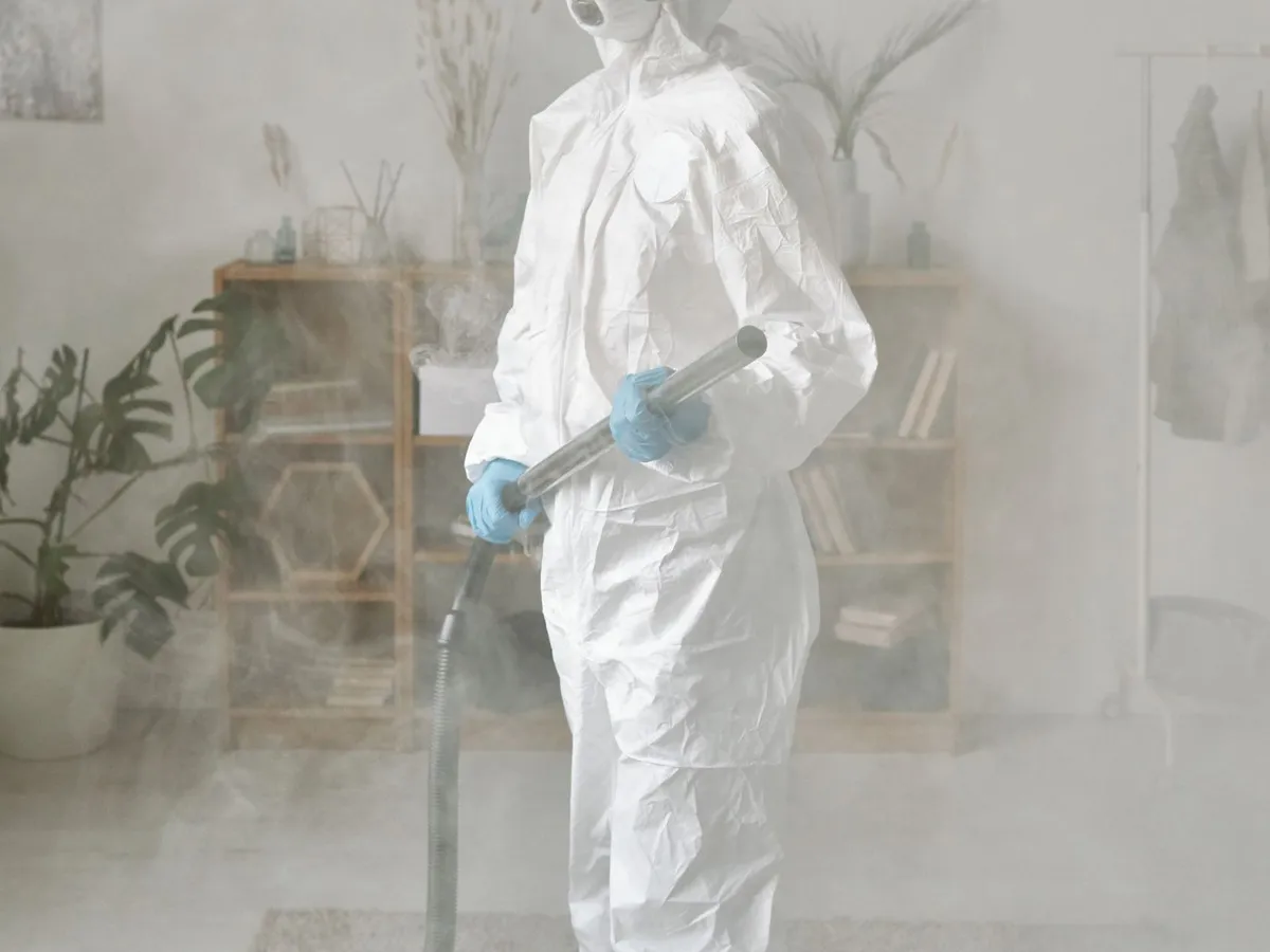 Worker in a protective suit treating a room filled with fog