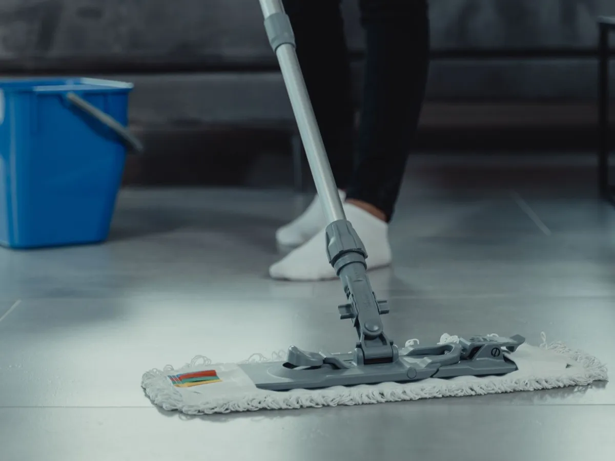 Person mopping a tile floor in a living room with a cleaning bucket nearby