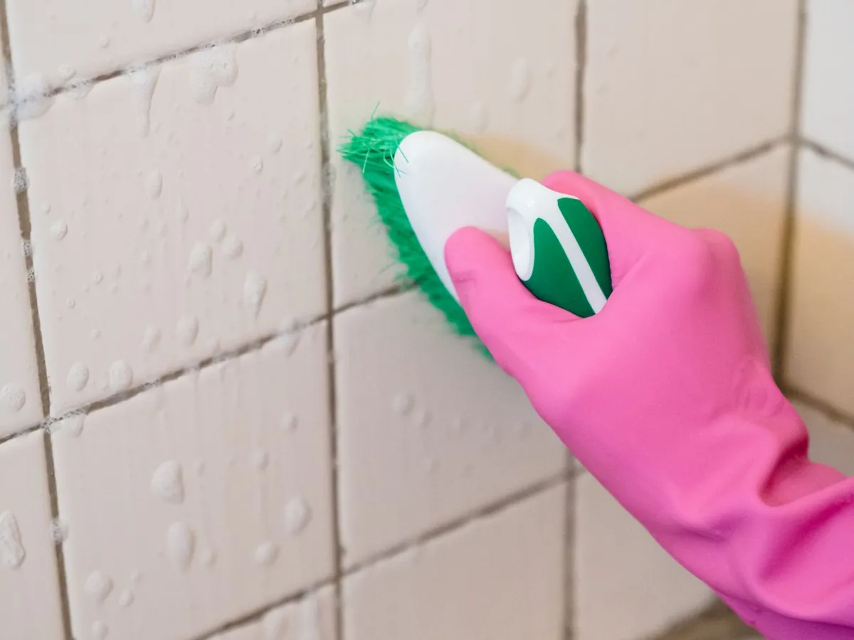 Gloved hand scrubbing tile grout with a brush